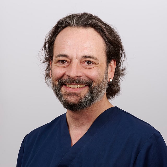 Une personne avec une barbe et une chemise bleue.